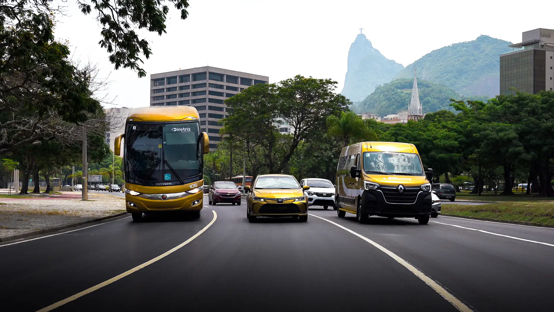 Ônibus, carro executivo e van do Grupo Braslectra na avenida, com o Cristo Redentor ao fundo